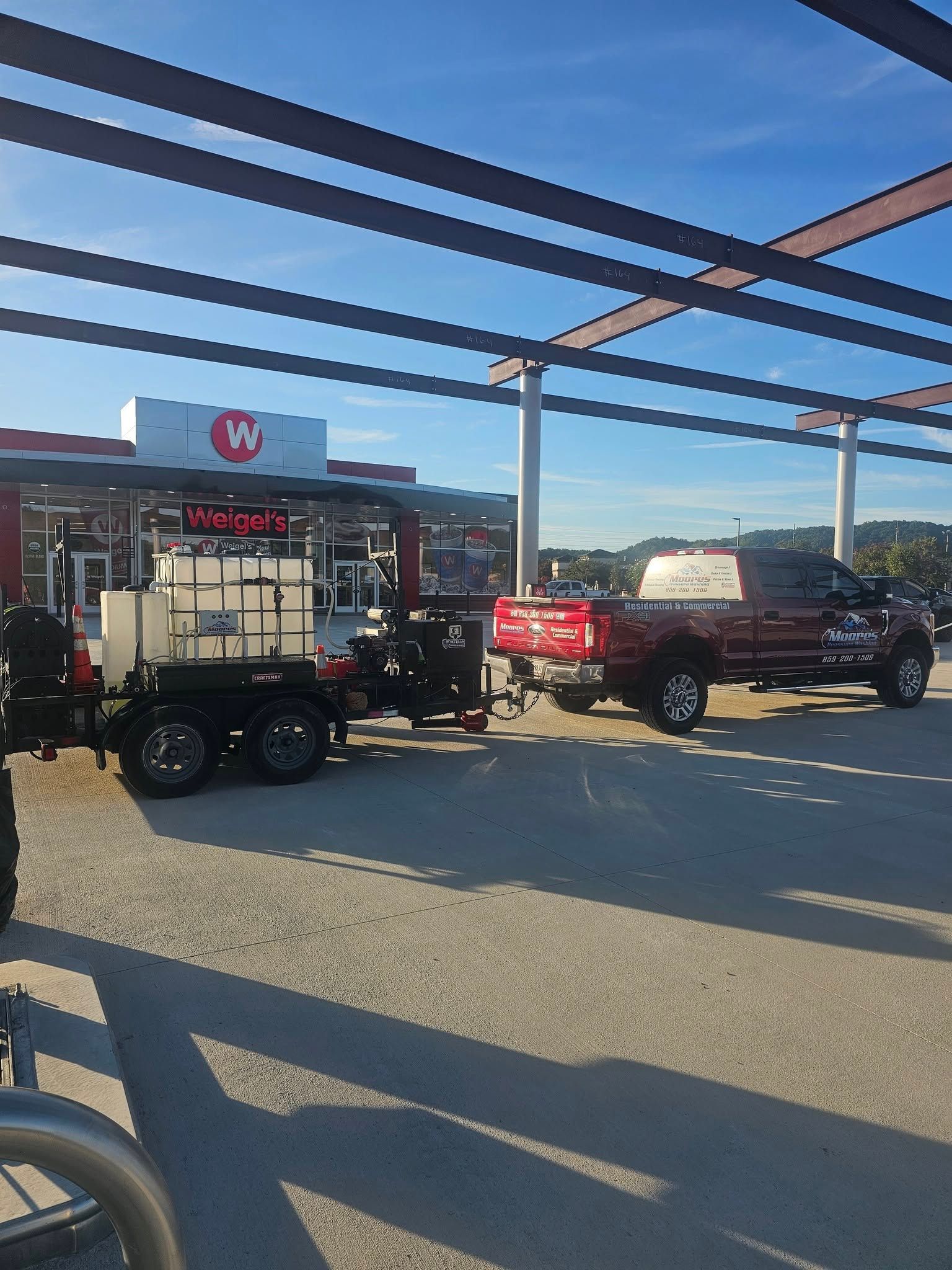 Two trucks parked outside a store under a metal canopy on a sunny day