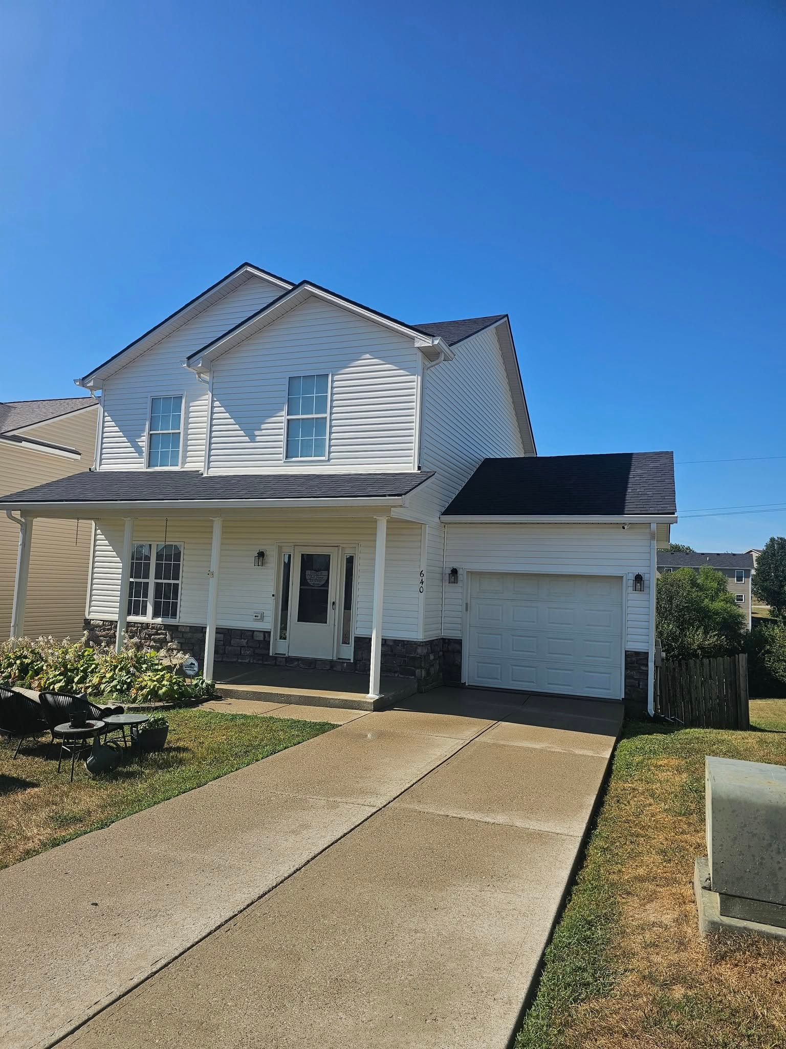 Two-story white house with a front porch, driveway, and attached garage under a clear blue sky