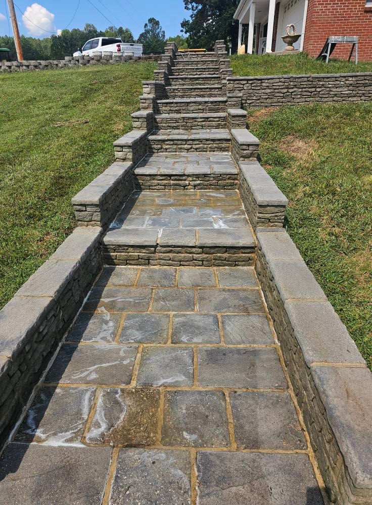 Stone walkway with multiple steps leading up a grassy slope beside a brick house.