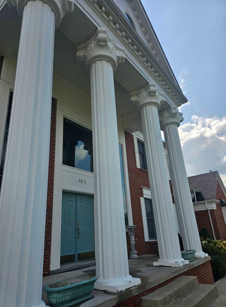Brick house with tall white columns and a teal front door under a cloudy sky.
