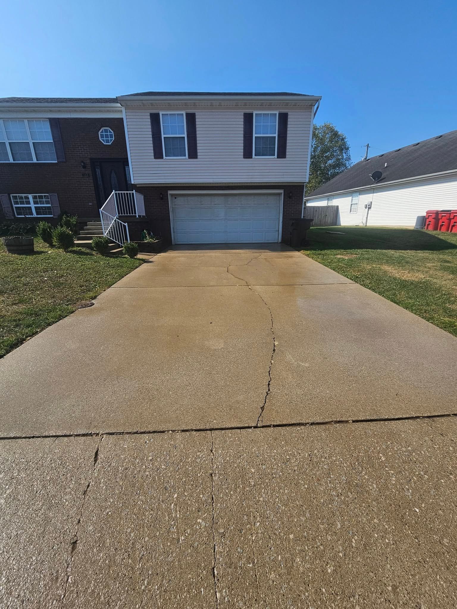 Suburban house with a long concrete driveway, garage, and green lawns under a clear blue sky