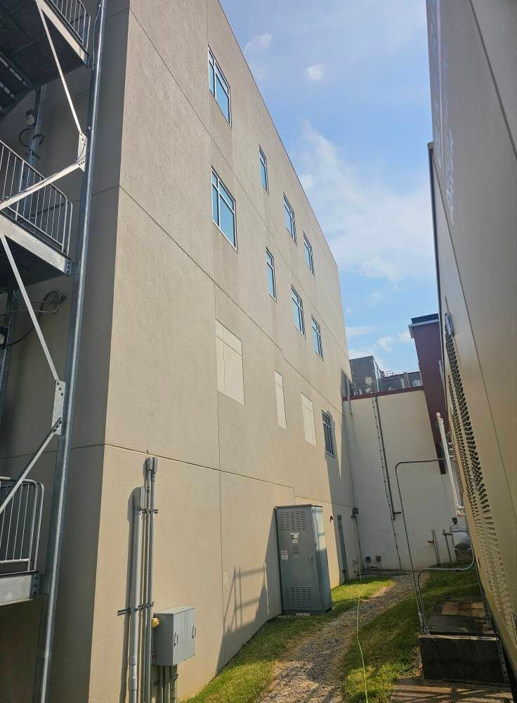 Narrow alley between beige apartment buildings with exterior stairs and utility boxes under a blue sky