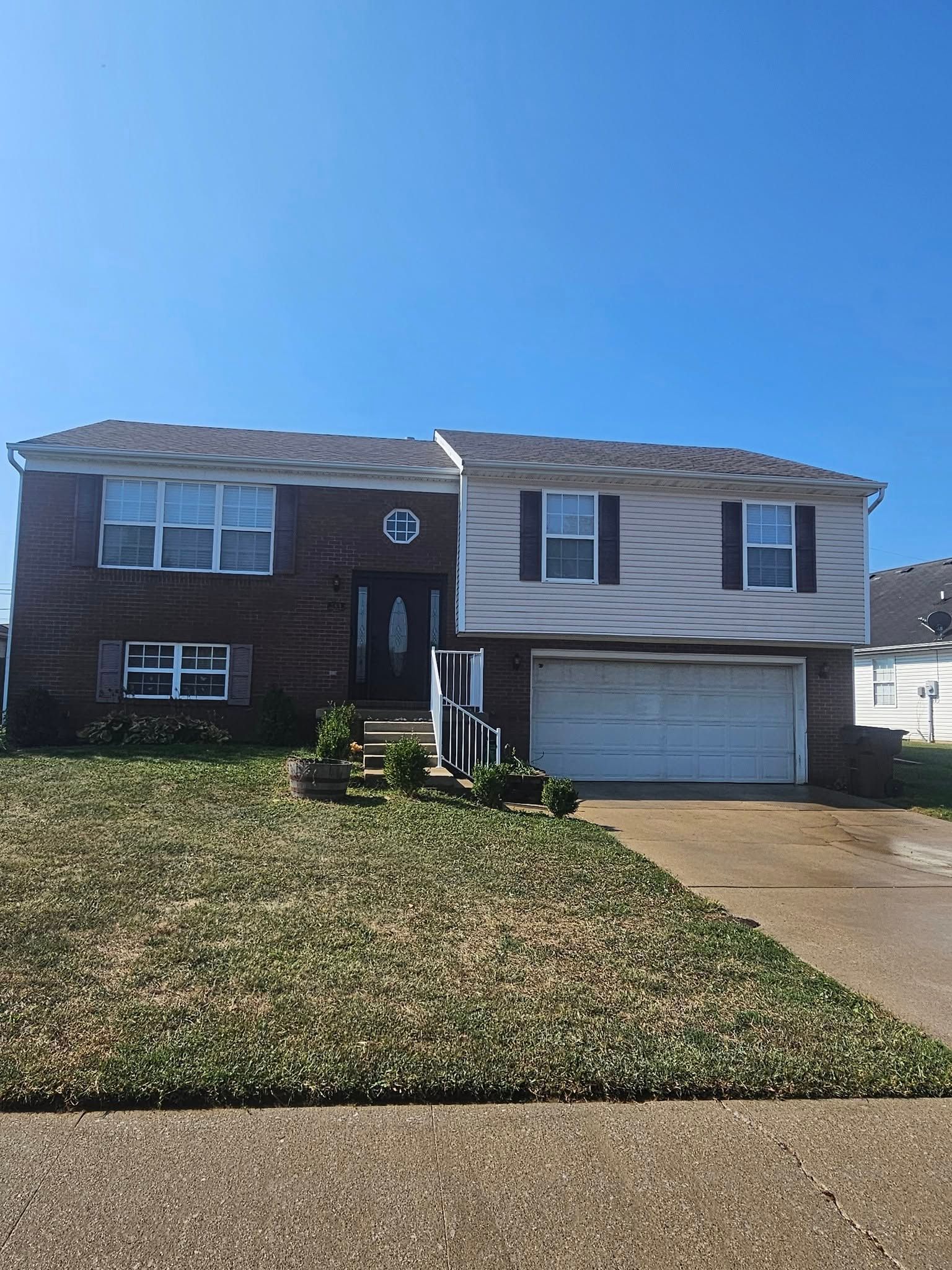 Suburban split-level house with a garage, brick and siding exterior, and a front lawn under a clear sky