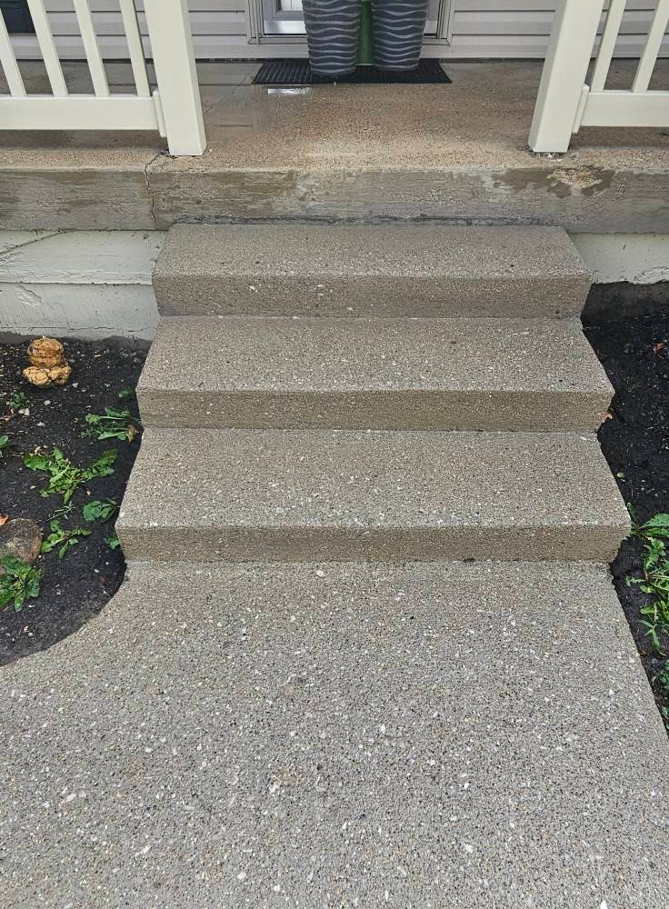 Concrete steps leading to a front porch with white doors and a small flower bed beside them