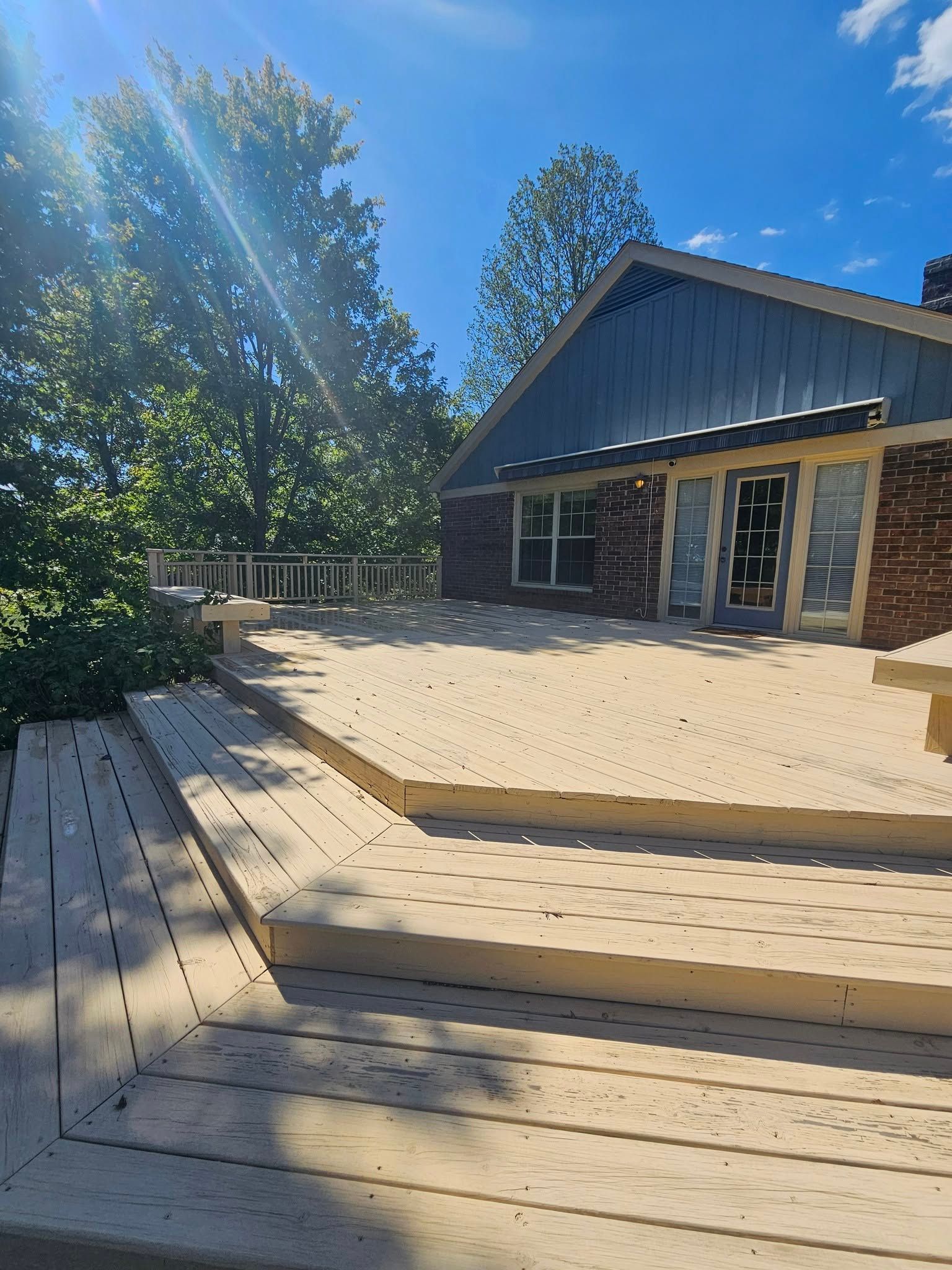 Wooden deck beside a rustic cabin in bright sunlight, with trees and blue sky in the background.