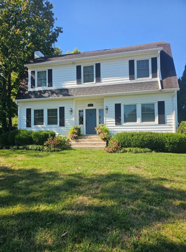 Two-story white house with blue shutters and a front lawn on a sunny day