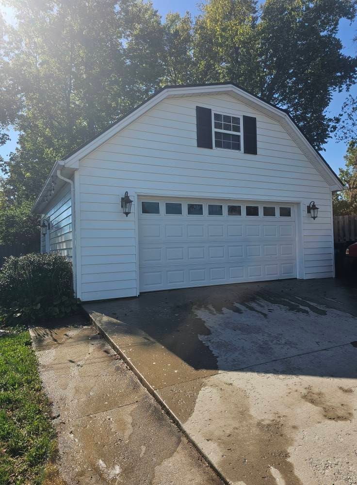 White detached garage with a black-trim window, driveway in front, and bright sunlight overhead.
