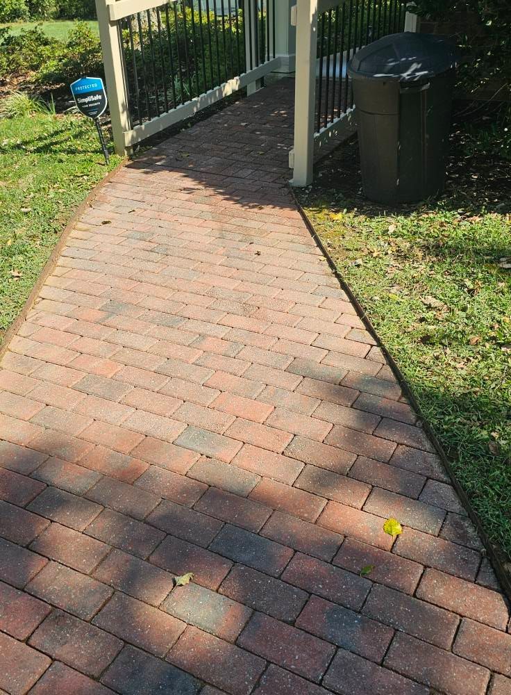 Brick walkway leading to a shaded porch with stairs and a grill in the yard