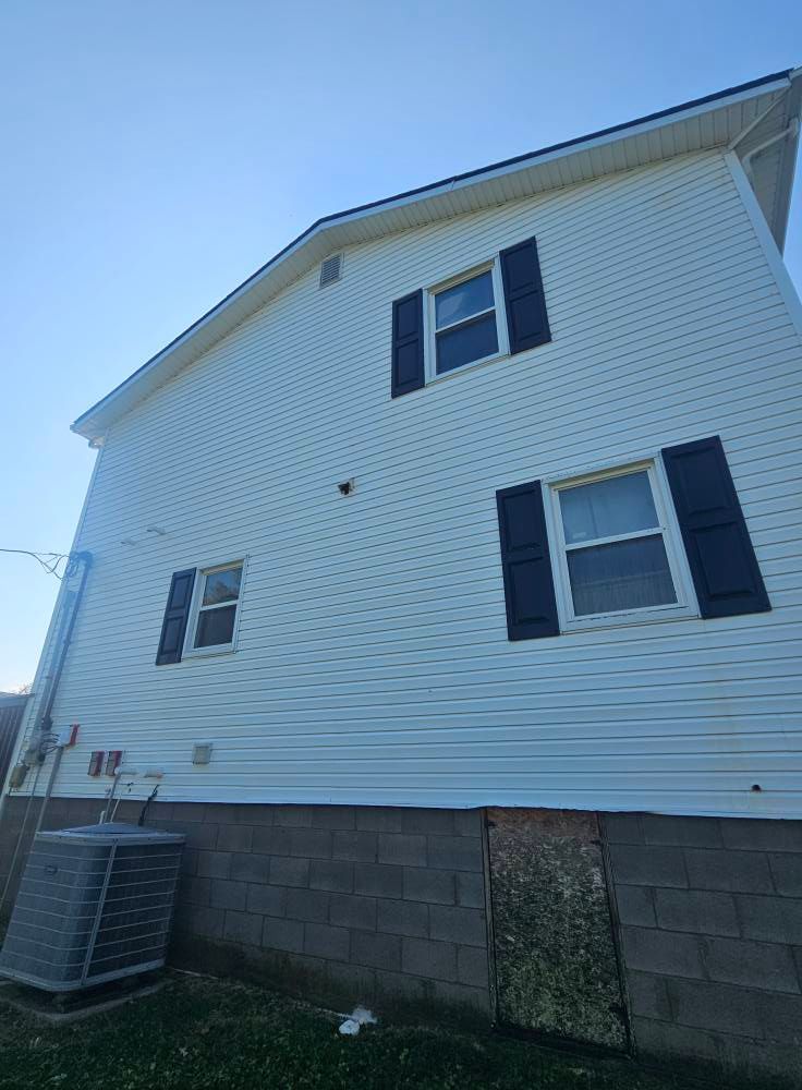 White vinyl house exterior with dark shutters, cinder block foundation, and an air conditioner unit on the left