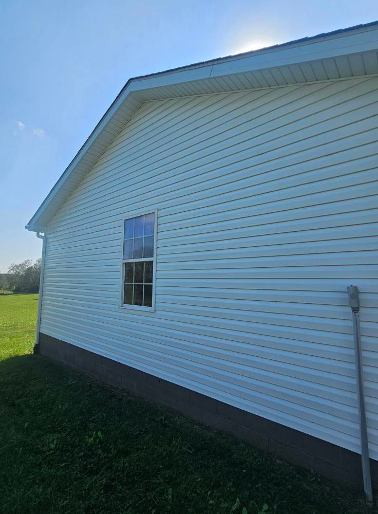 Side of a white vinyl house with a window and sloped roof under a blue sky.