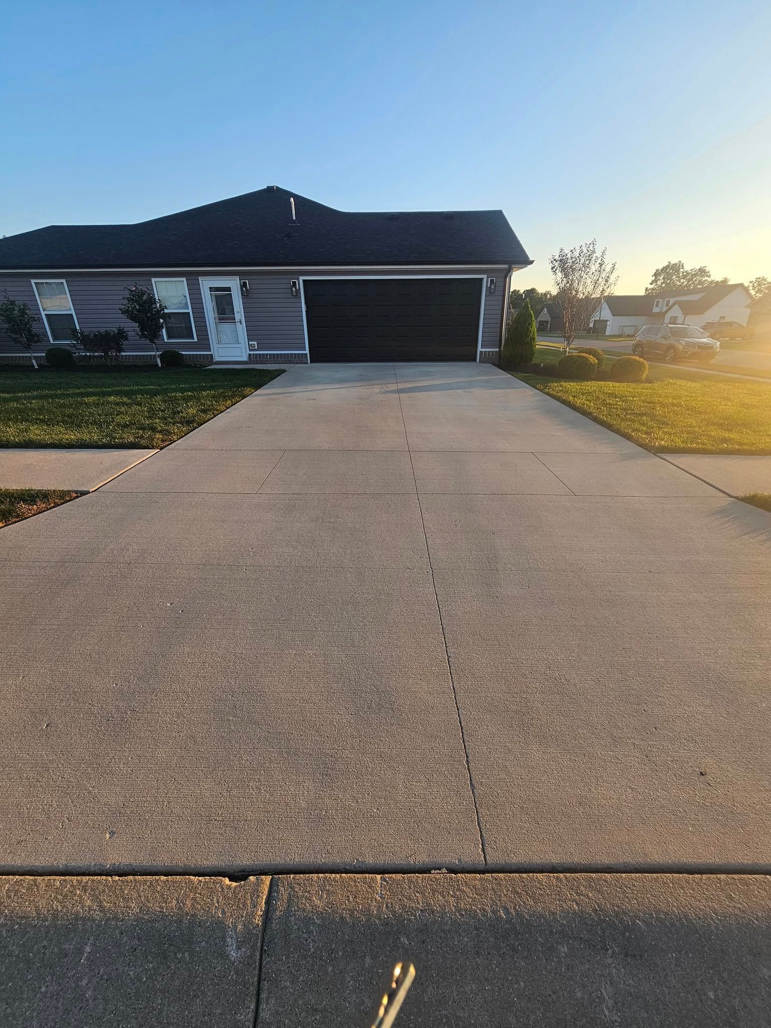 Suburban house with a long driveway leading to a garage at sunset