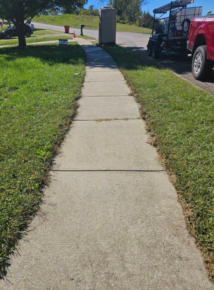 Concrete sidewalk leading to a road, with grass on both sides and a red truck parked on the right.