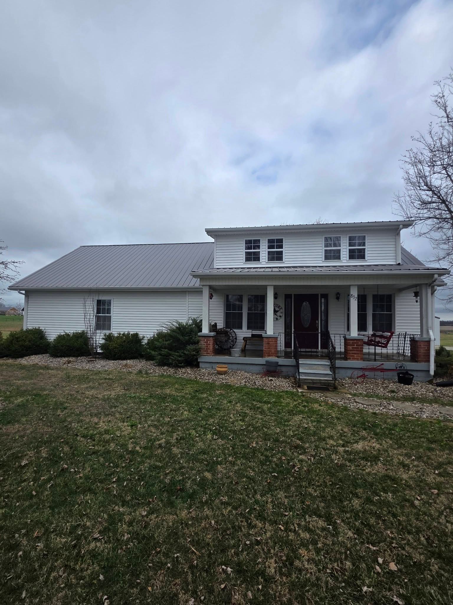 White farmhouse with a covered porch and leaf-covered lawn under a cloudy sky