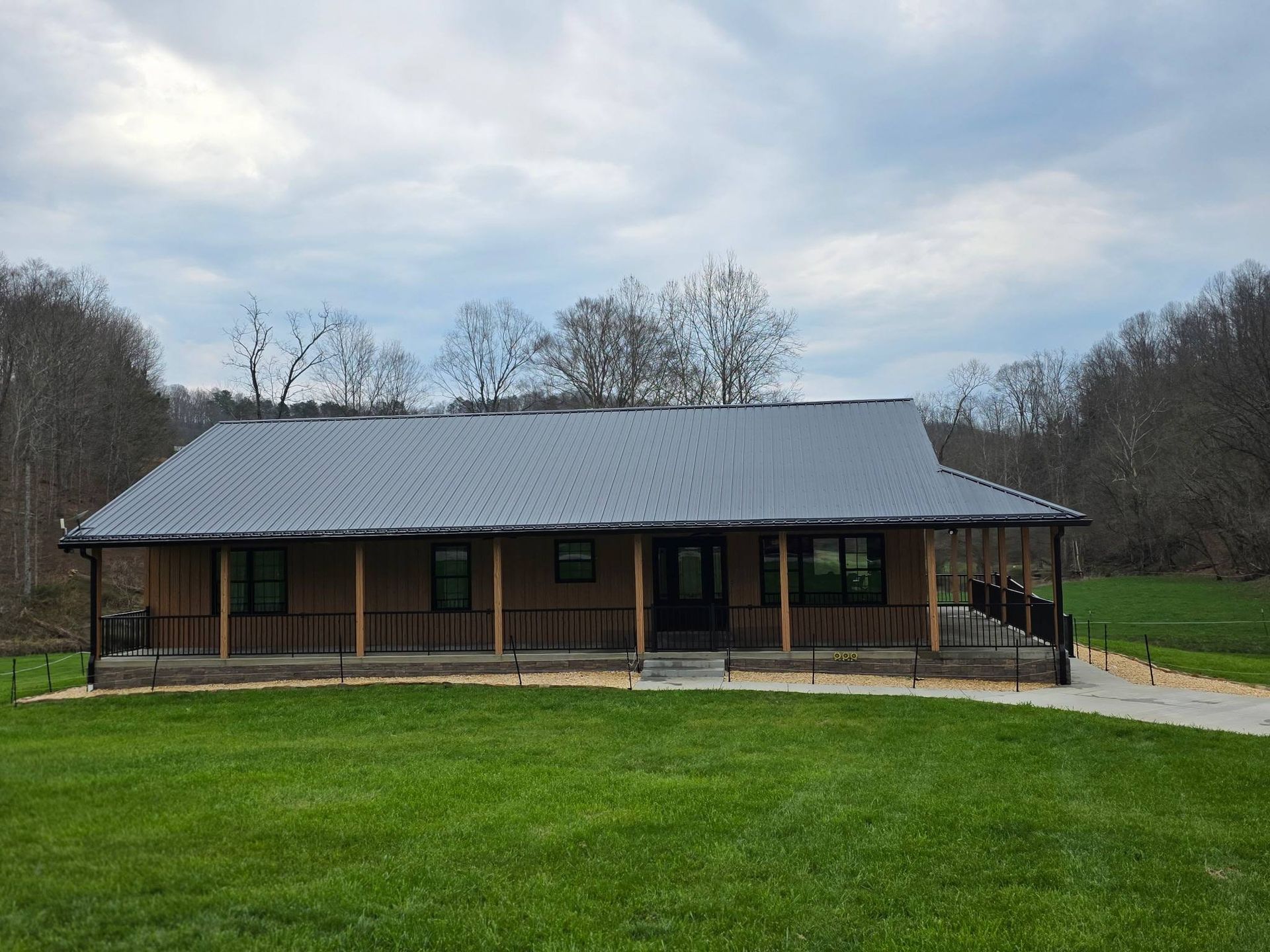 Single-story brick house with a gray metal roof and large green lawn in front.