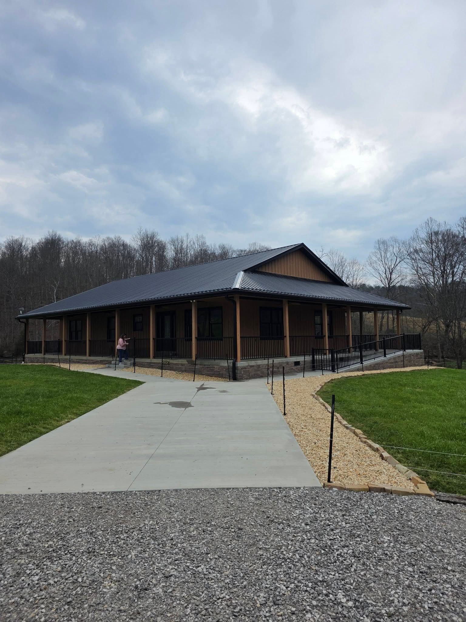 Modern wooden building with a sloped roof, front porch, and concrete path under a cloudy sky