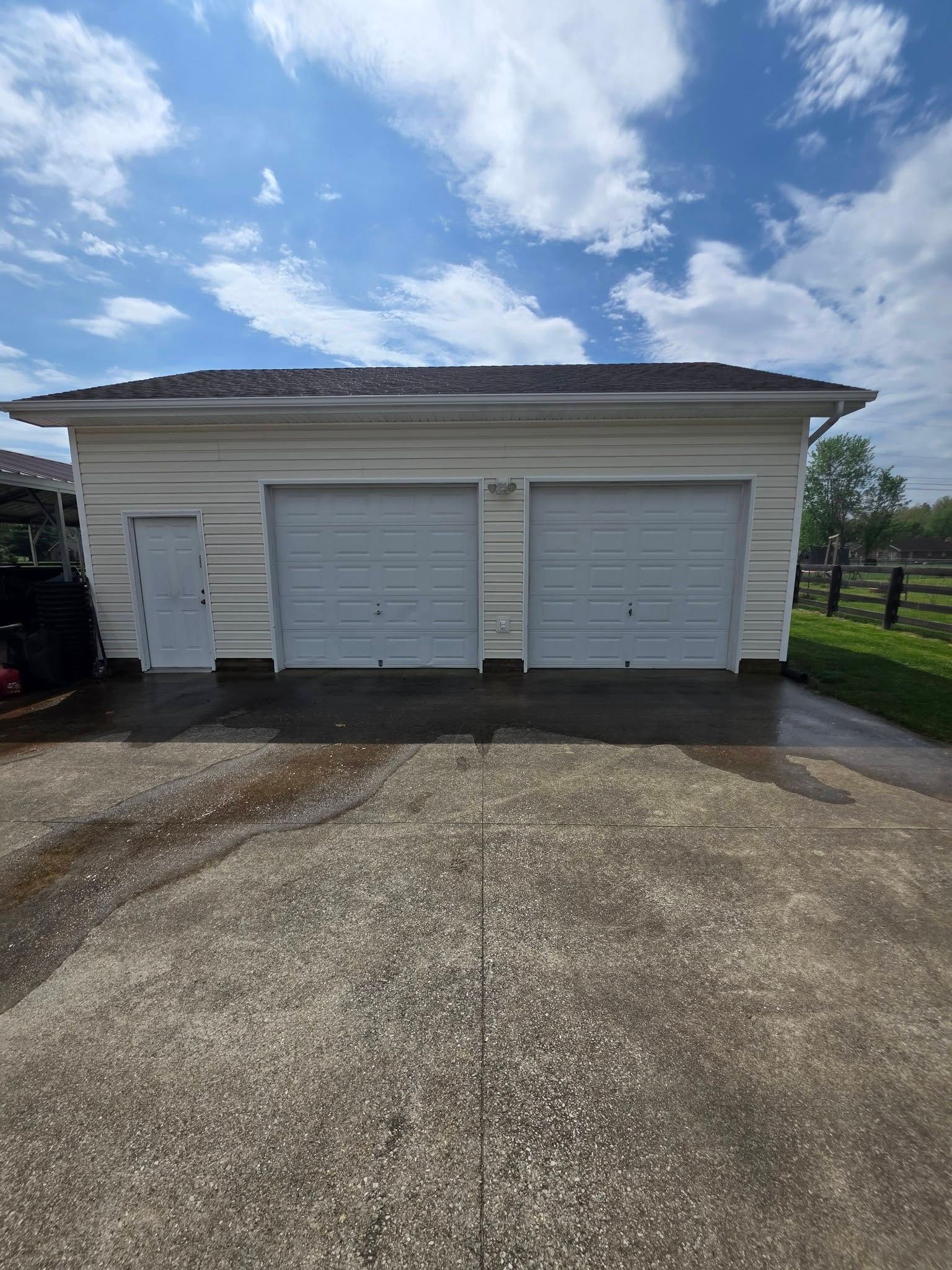 Single-story garage with two white doors and a driveway under a partly cloudy sky.