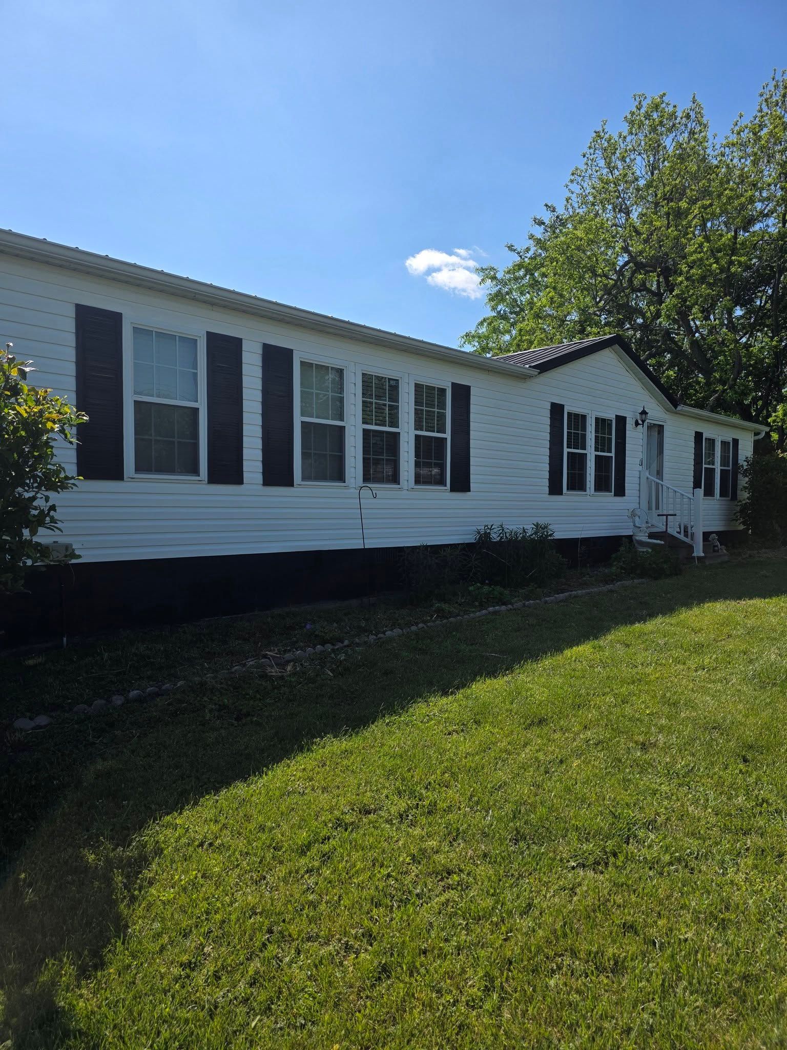 White single-story house with dark shutters and green lawn under a blue sky