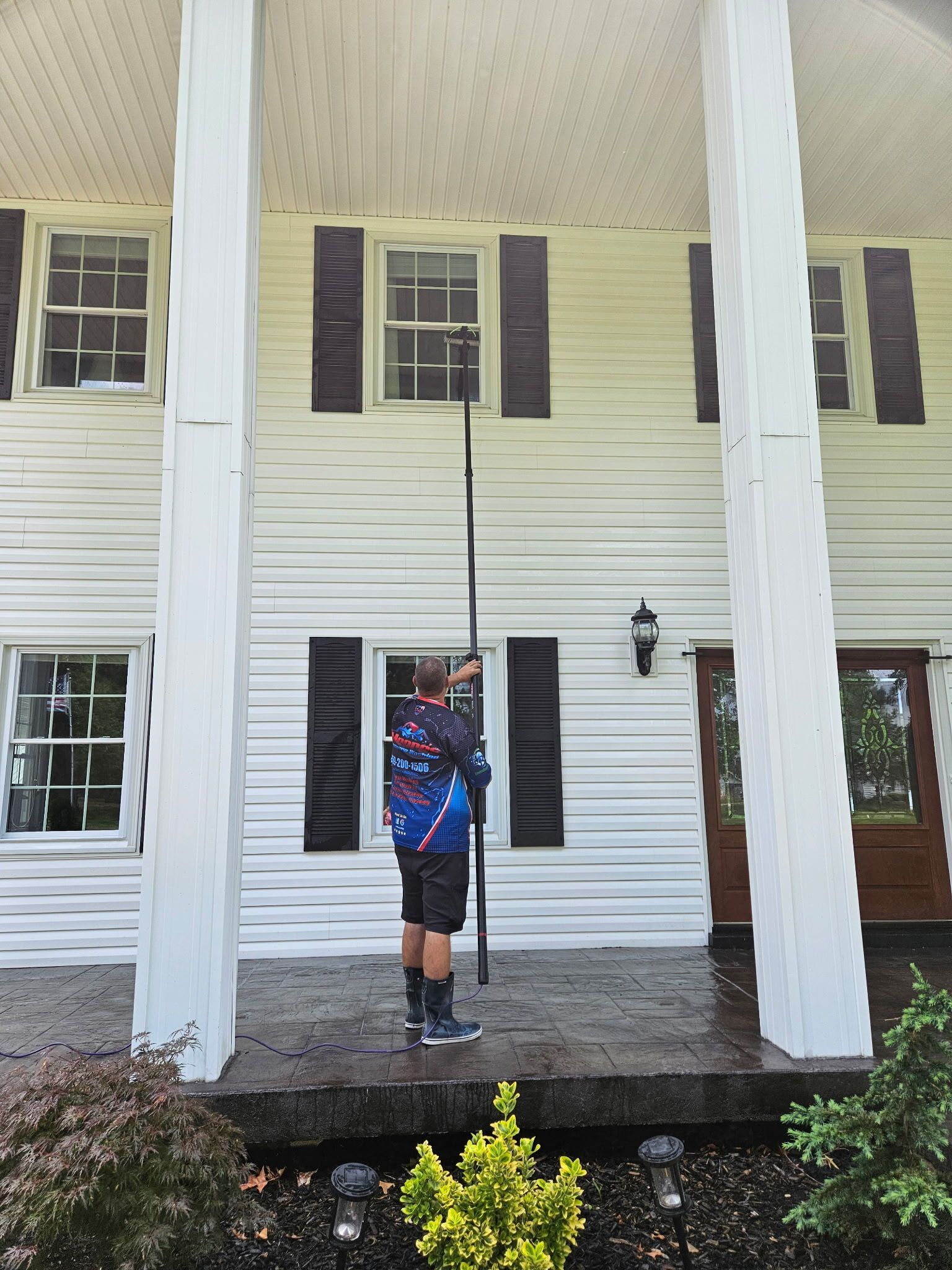 Person standing on a porch with white columns in front of a white house, holding something overhead