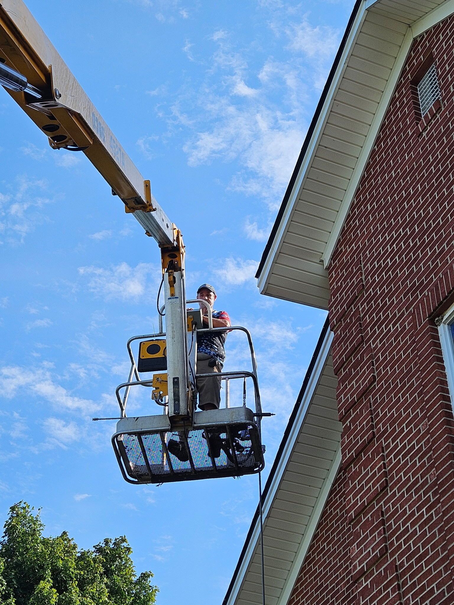 Workers in a cherry picker beside a brick building under a blue sky