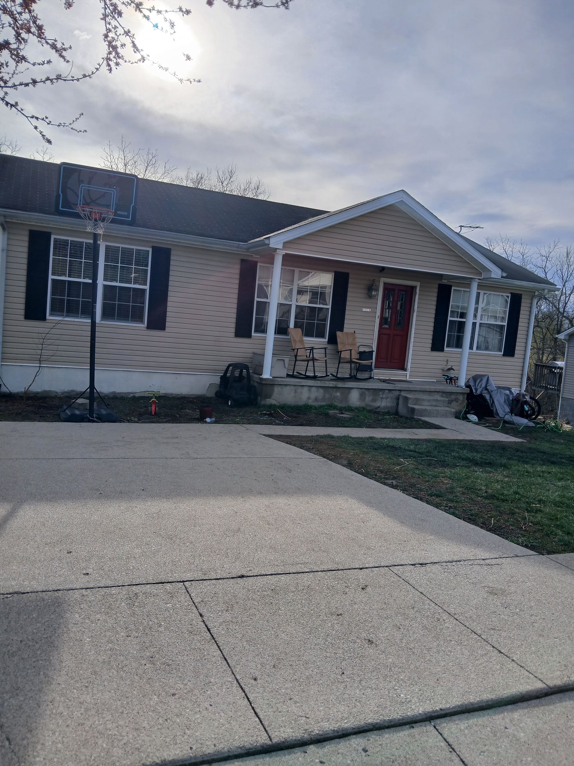 Single-story beige house with a front porch, red door, and driveway in the foreground
