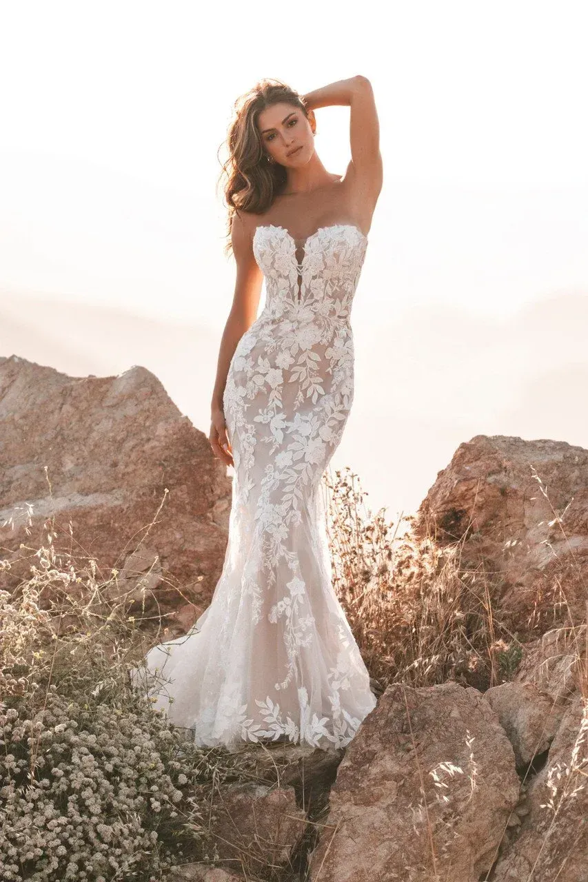 Woman in white strapless lace wedding dress, posing on rocks, with sunlight in the background.