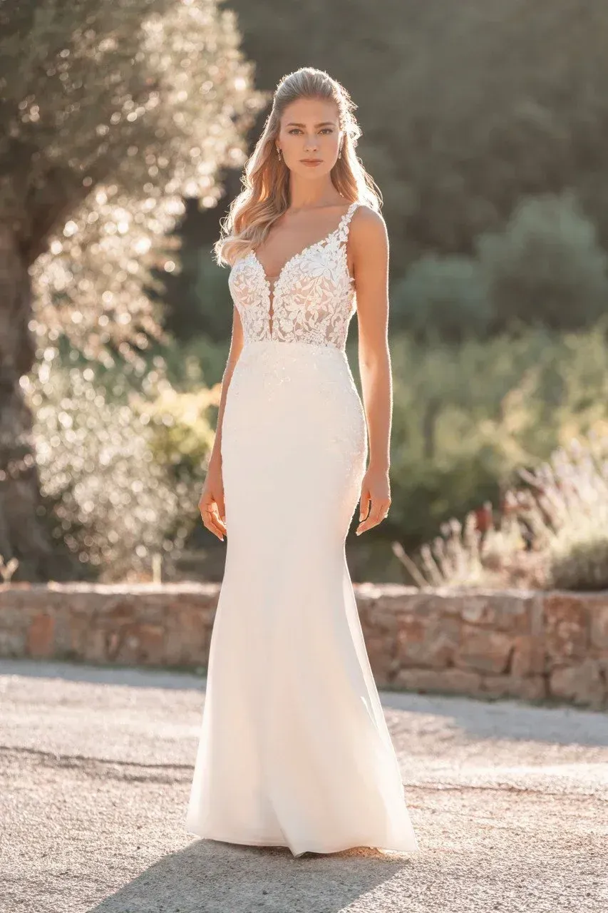 Woman in a white wedding dress poses outdoors; lace bodice, fitted silhouette.