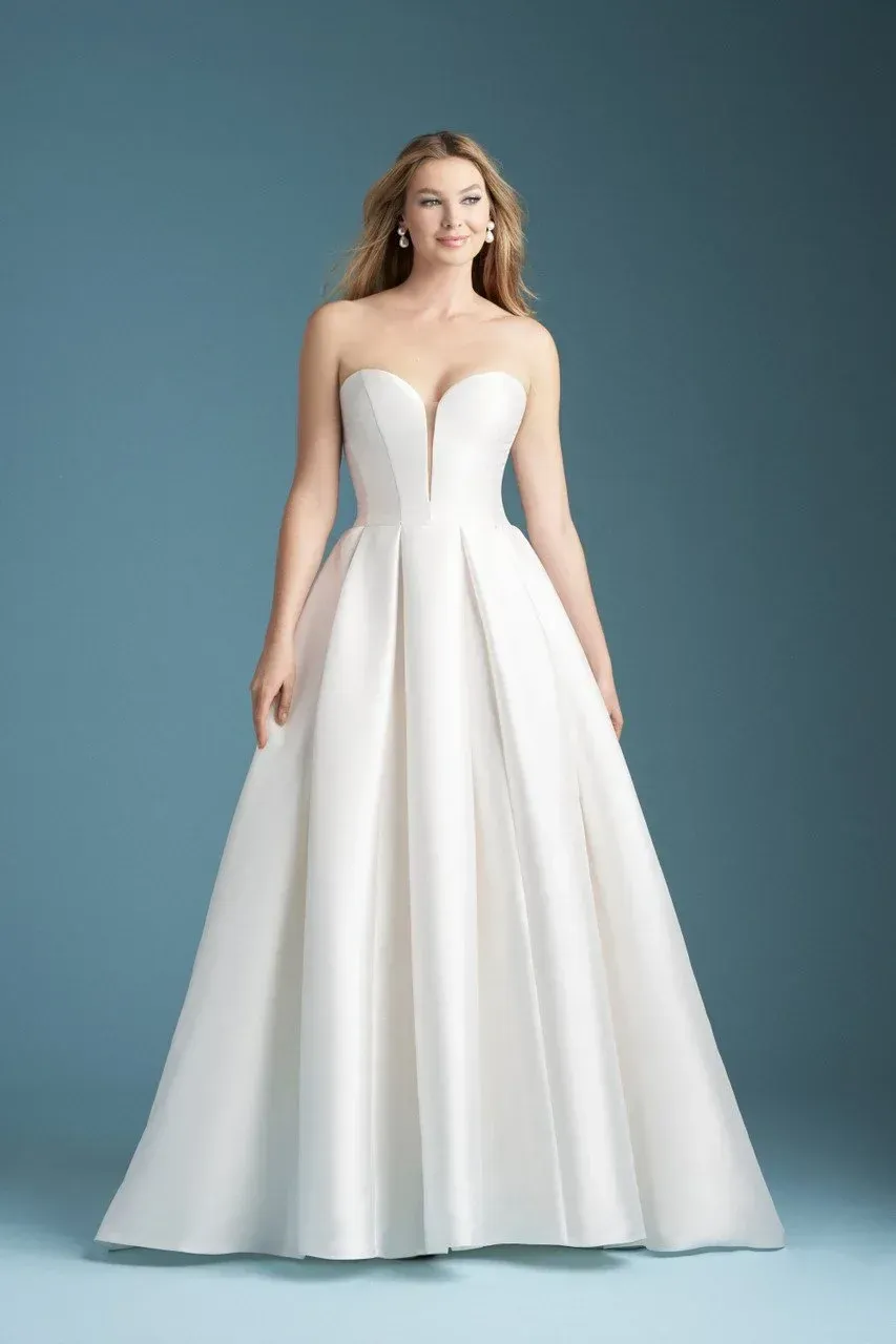 Woman in a strapless white wedding dress with a sweetheart neckline, standing in front of a blue backdrop.