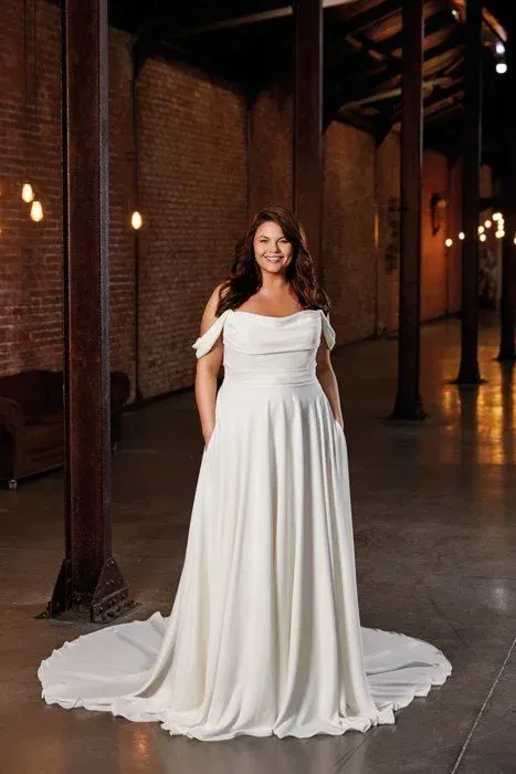 Woman in a white wedding dress, smiling, standing in a rustic building.