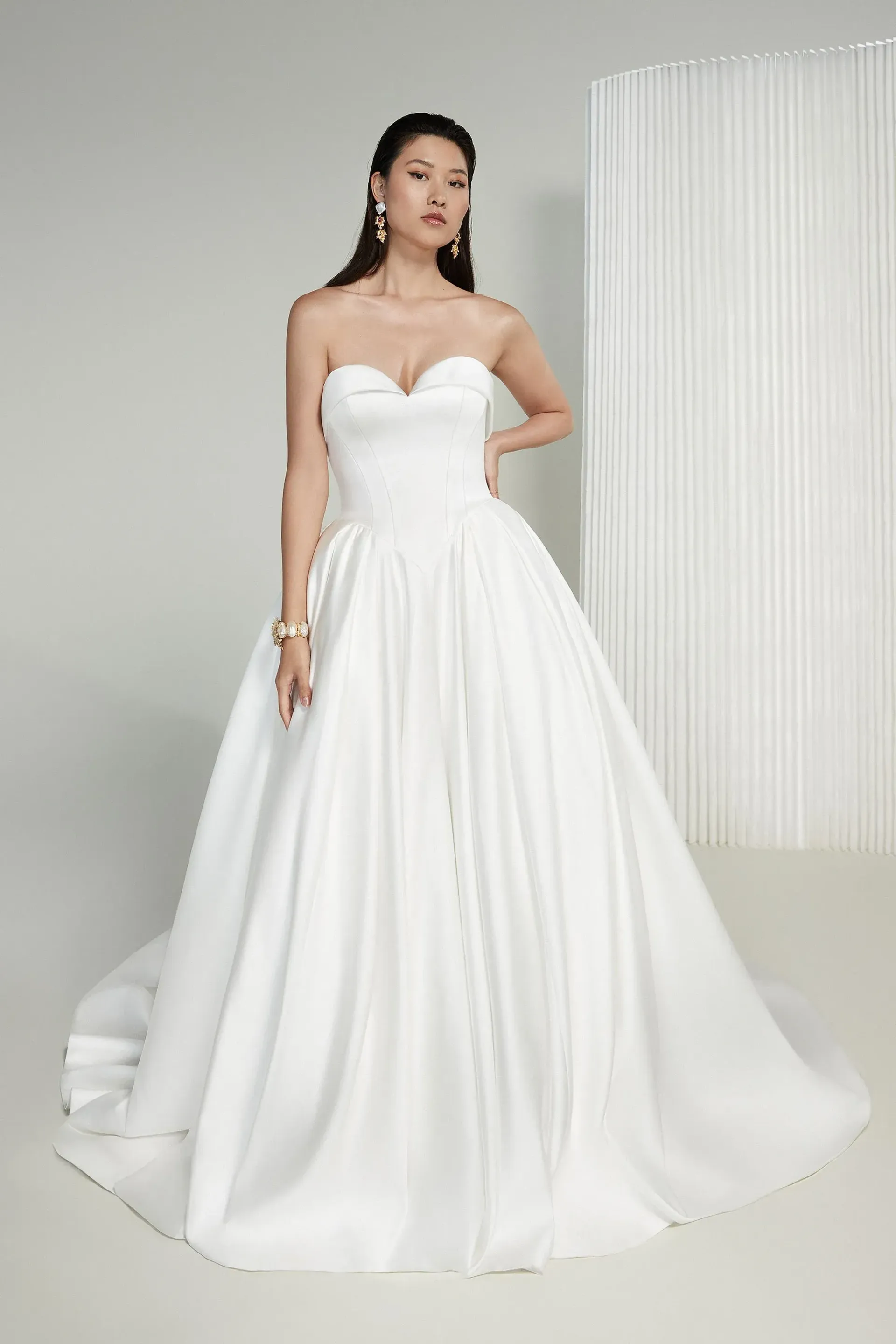 Woman in a white strapless wedding dress, posing in a studio with a white backdrop.