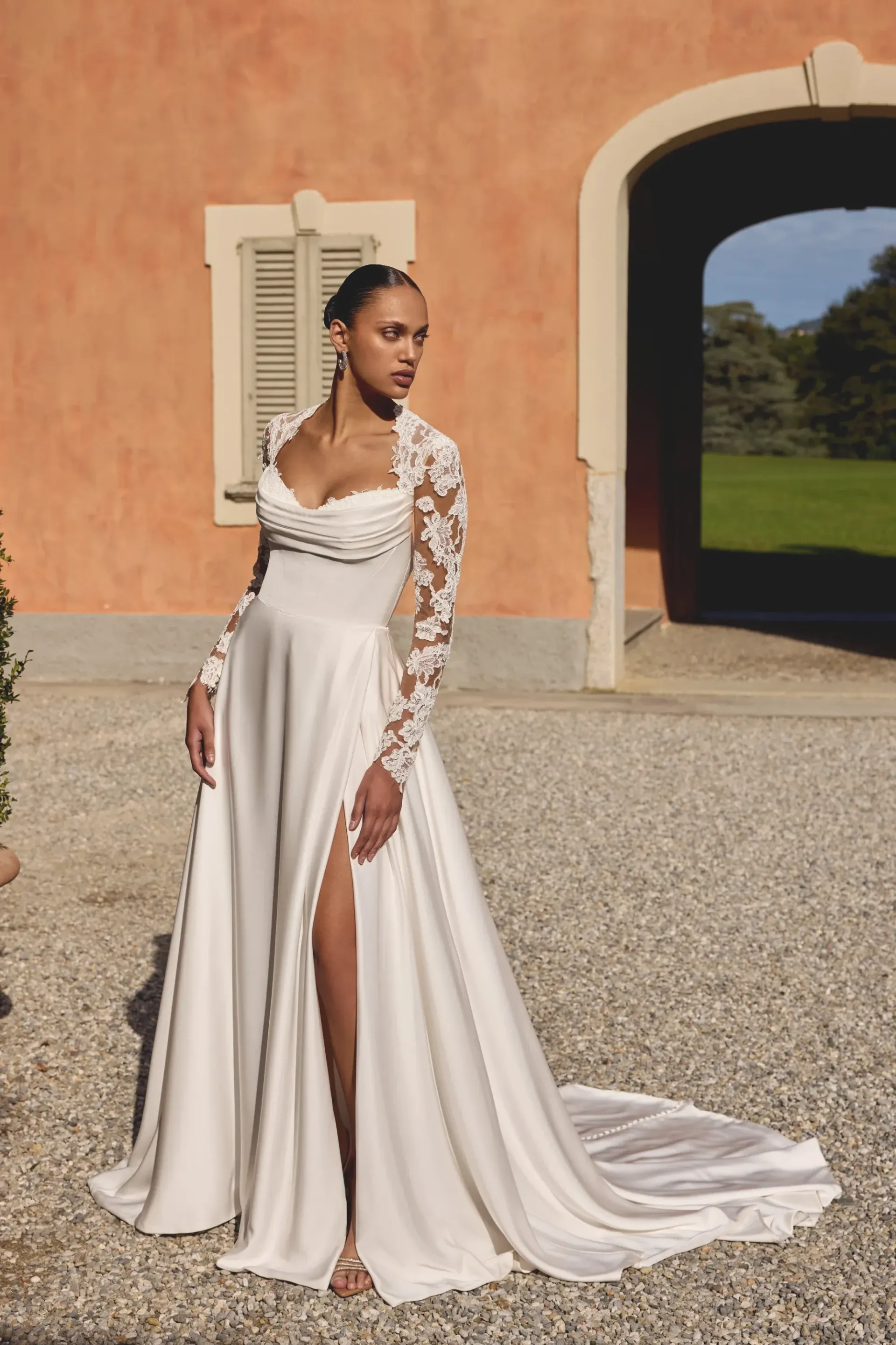 Woman in a white wedding dress with a high slit posing outdoors, with a floral lace sleeve.