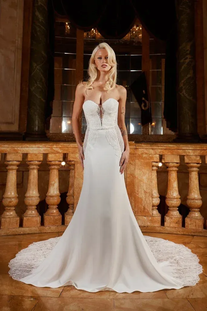 Blonde woman in a white strapless wedding gown with lace train, posing in a stately room.