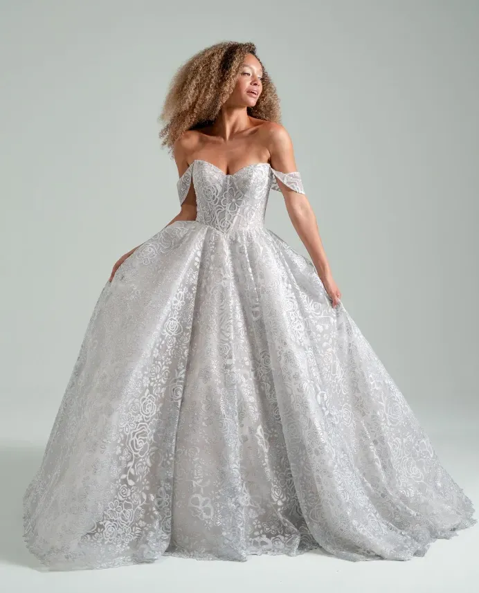 Woman in a silver off-the-shoulder ballgown. She's smiling, standing in a studio setting.