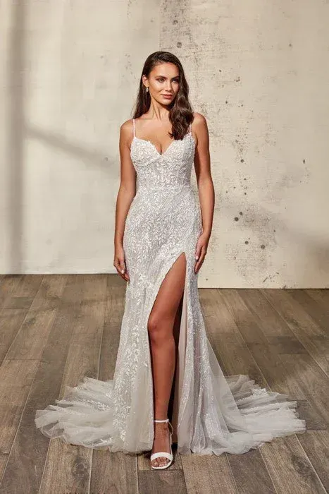 Woman in a white wedding dress with a thigh-high slit, standing on wooden floor.