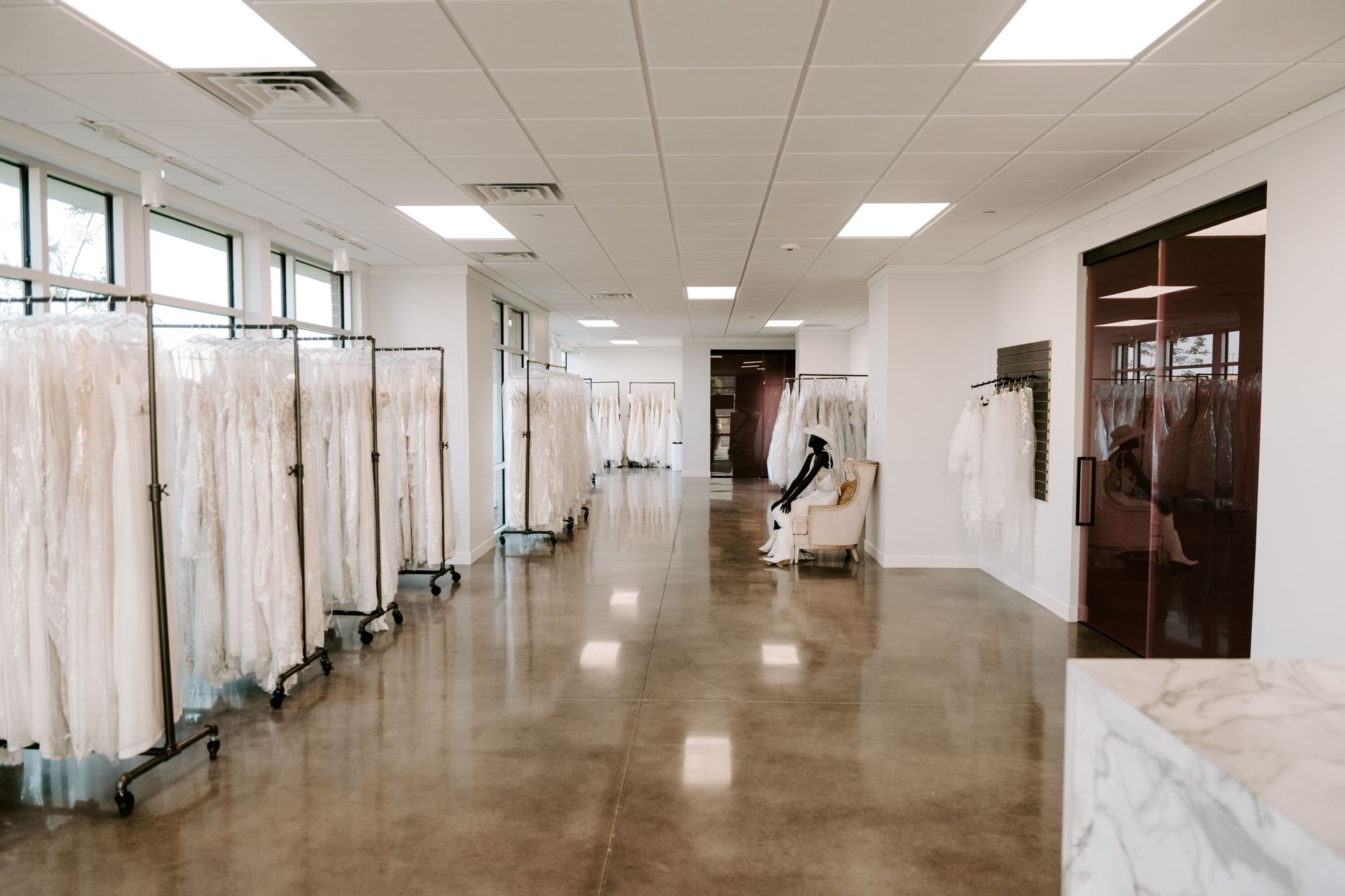 A wedding dress shop with white dresses hanging on racks, concrete floors, and bright lighting.