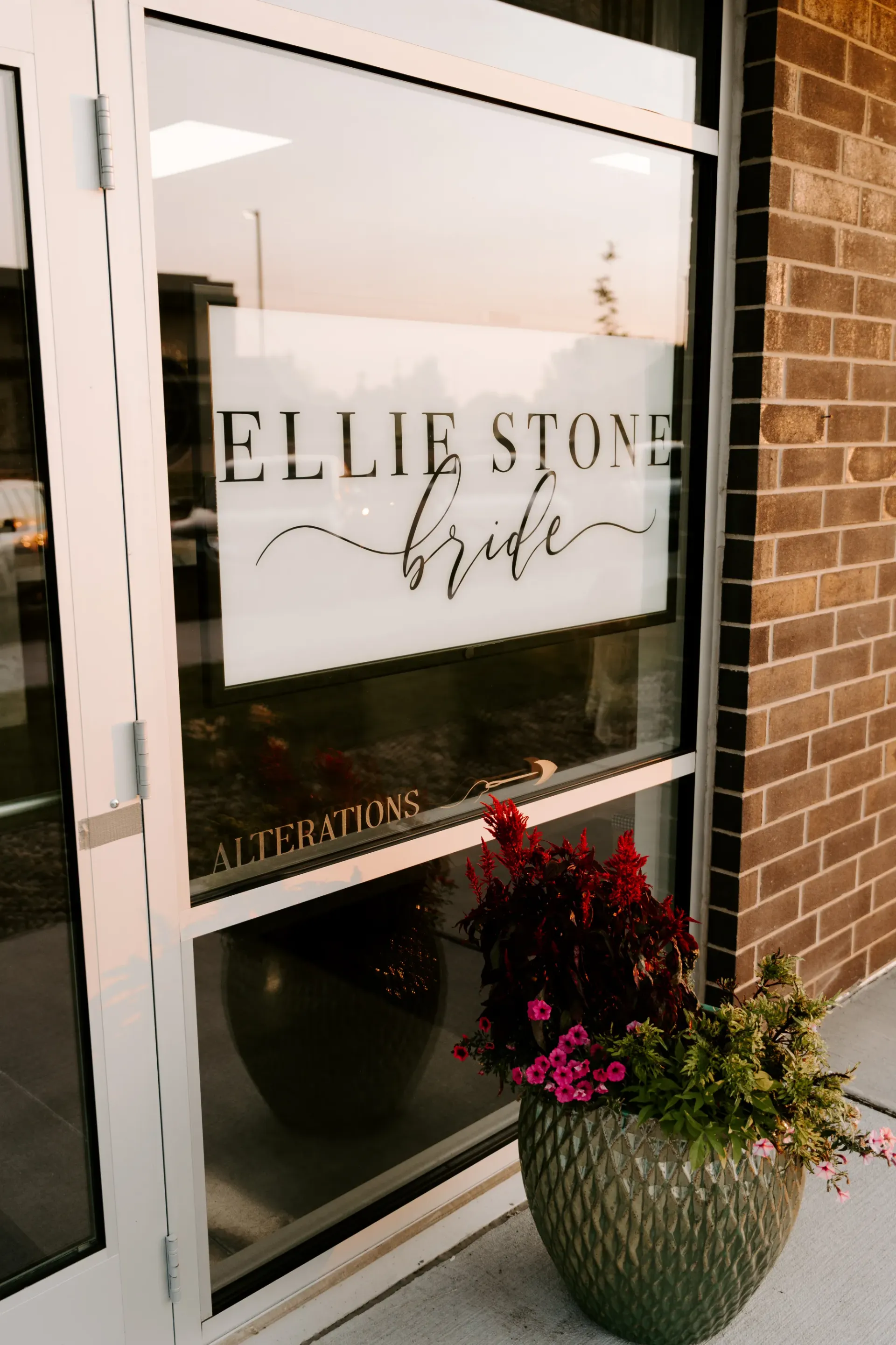Ellie Stone Bride storefront window with a logo. A potted plant sits outside the door against a brick building.