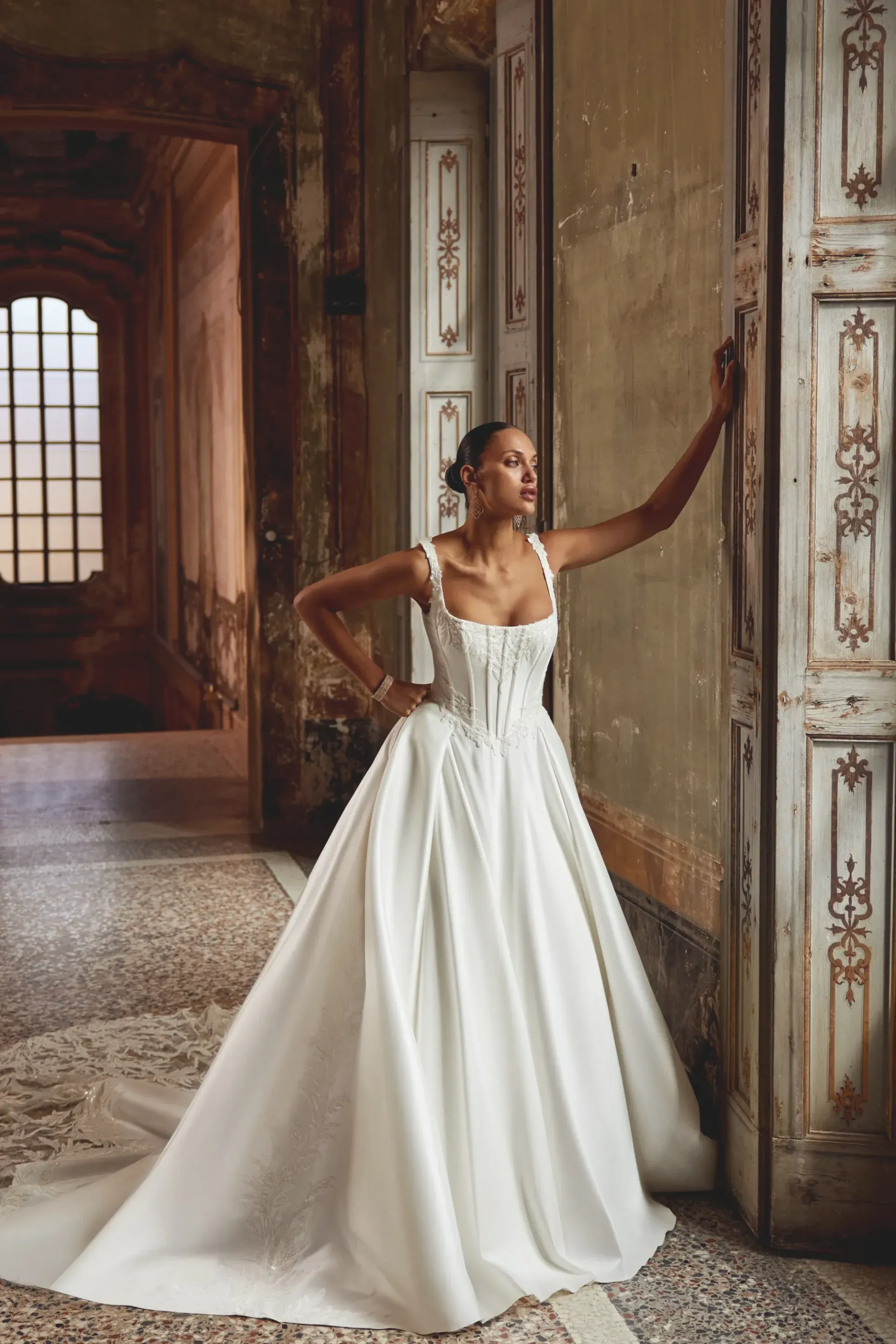 Woman in white wedding dress poses in an ornate, aged doorway.