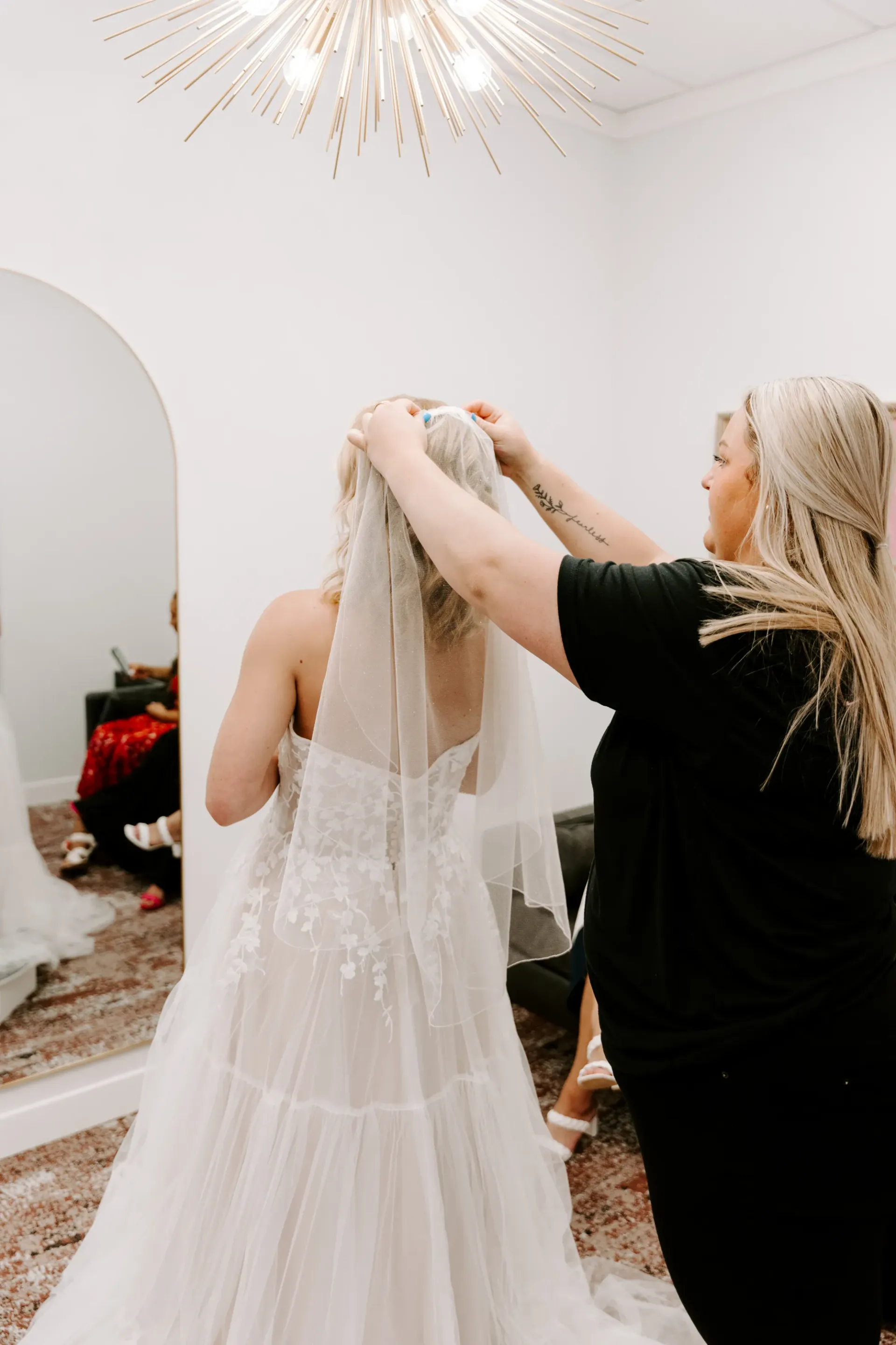 Woman in wedding dress having veil adjusted by another woman in a bridal shop.