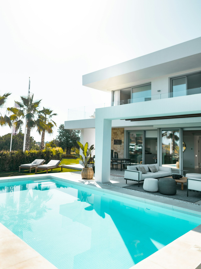 Modern white villa with turquoise pool, lounge chairs, and glass doors in a sunny backyard