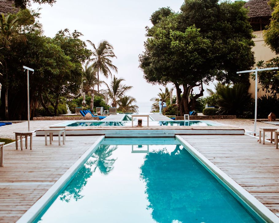 Outdoor resort pool with turquoise water, wooden deck, lounge chairs, and lush trees around it.