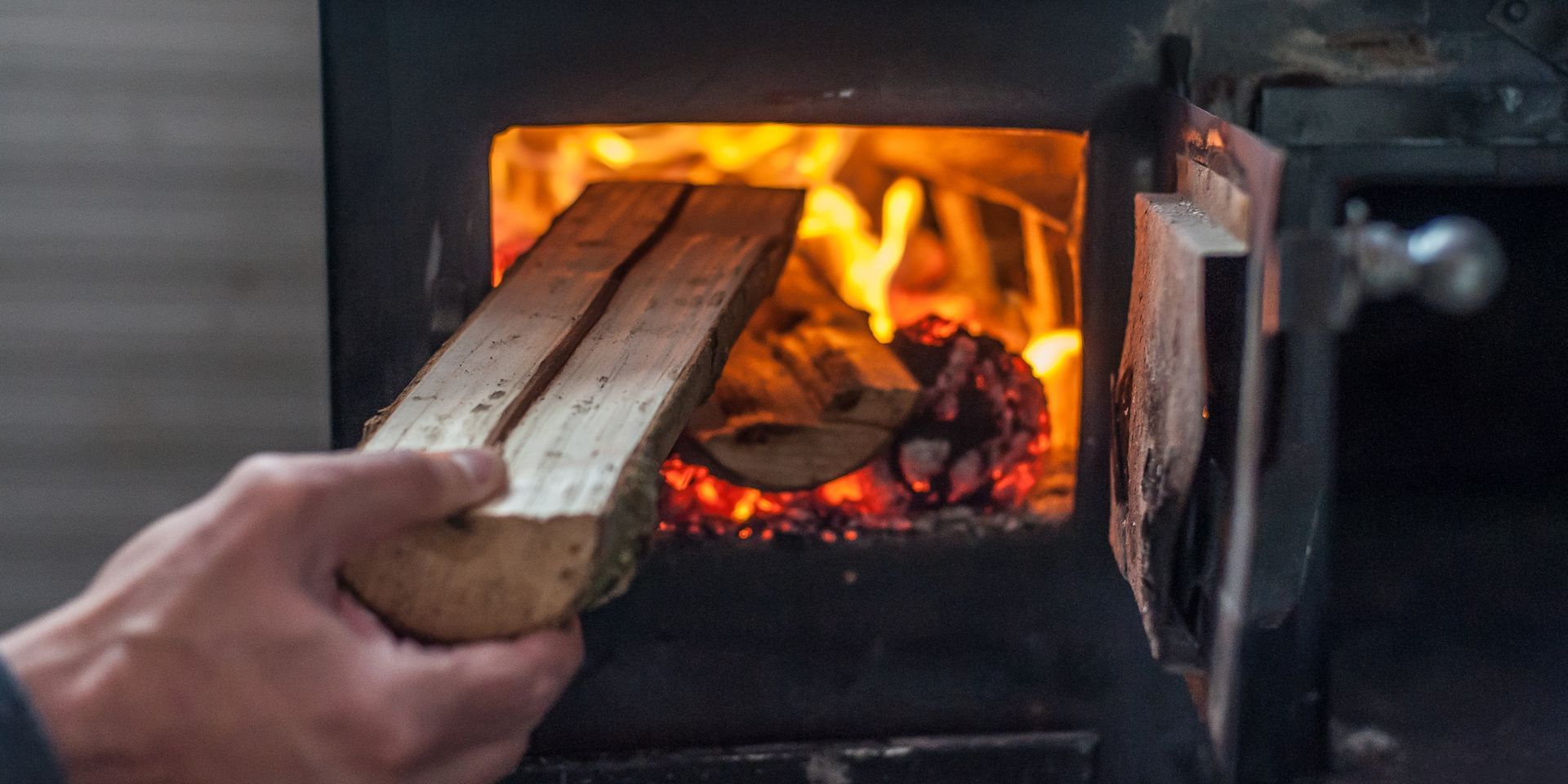 Man putting log to wood burning stove.