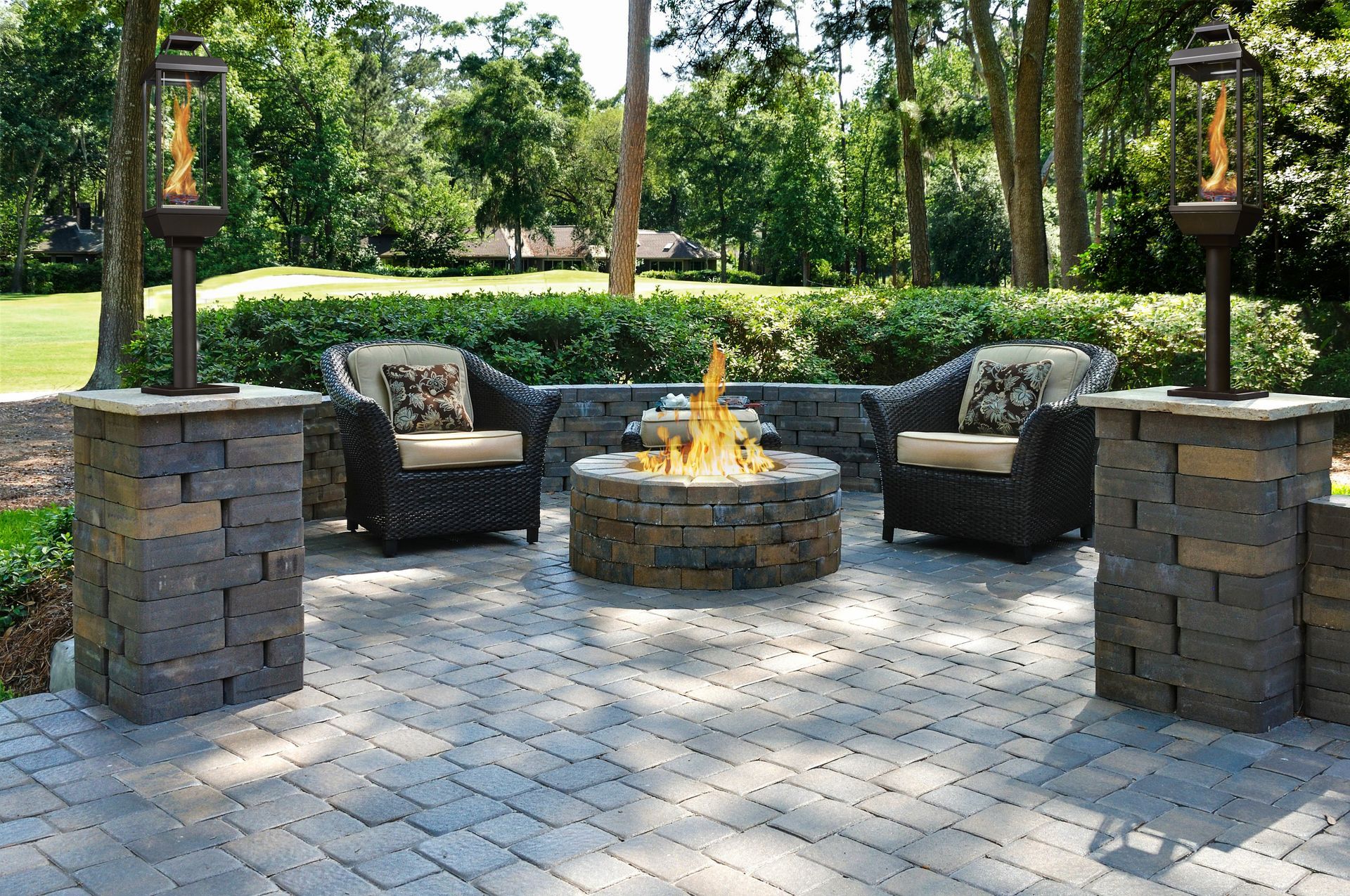 Stone patio with fire pit, cushioned chairs, and lanterns in a landscaped garden area