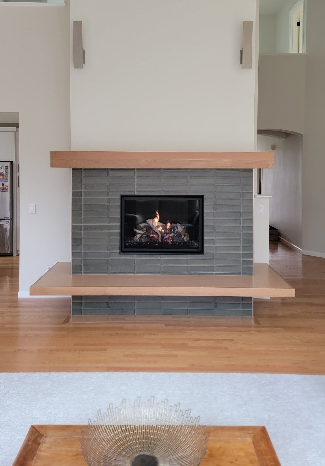 Living room with a modern tiled fireplace and wood mantle, viewed from across a hardwood floor.