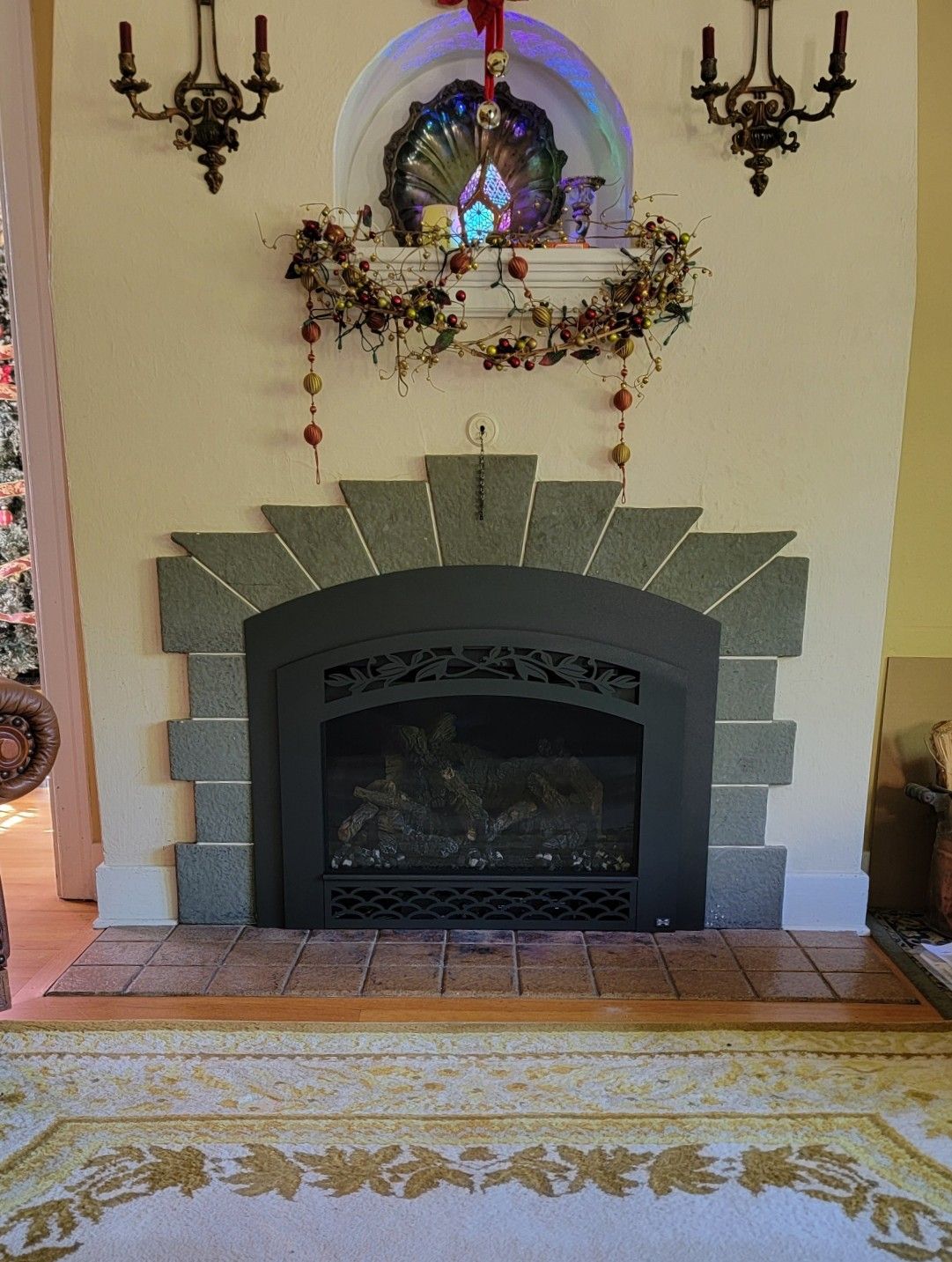 Living room fireplace with gray stone surround, wall sconces, and holiday mantel decor