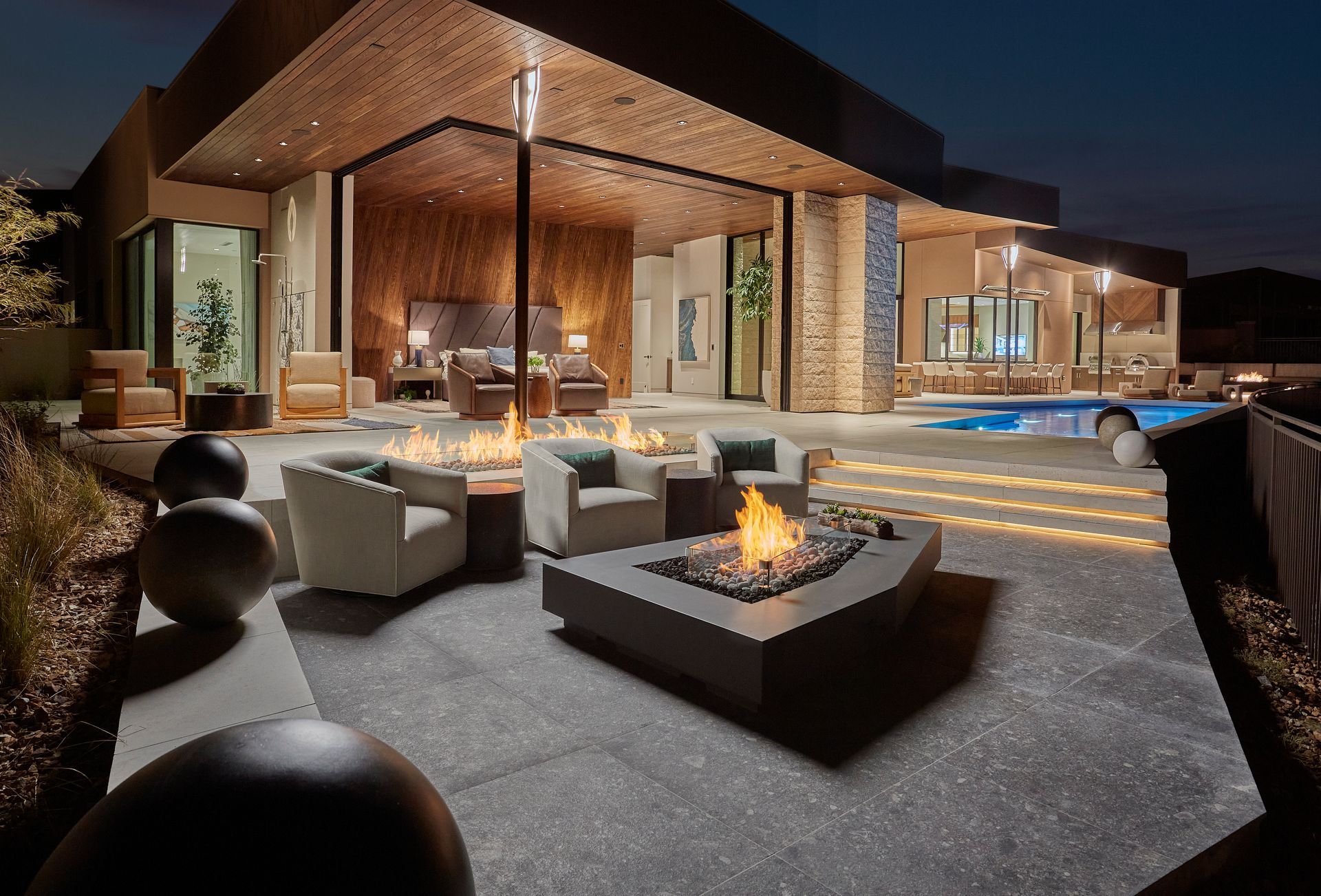 Modern luxury patio with fire pit, lounge seating, and a lit house at dusk