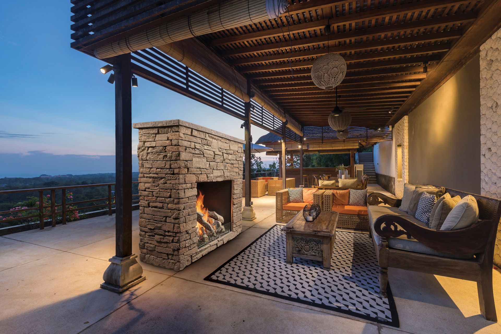 Covered stone patio with fireplace, wicker seating, and mountain sunset view
