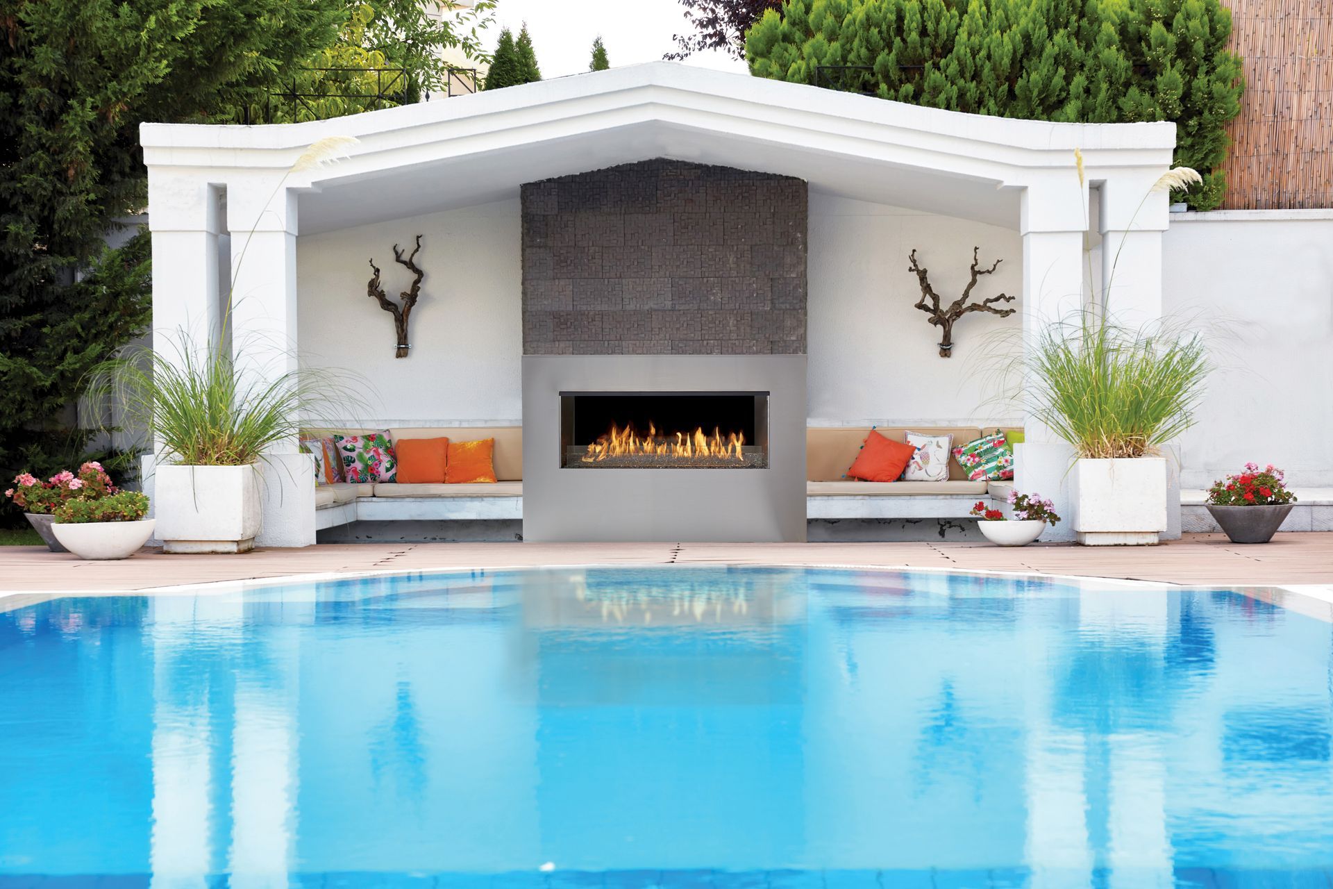 Modern backyard pool with a white cabana and built-in fireplace reflecting in the water