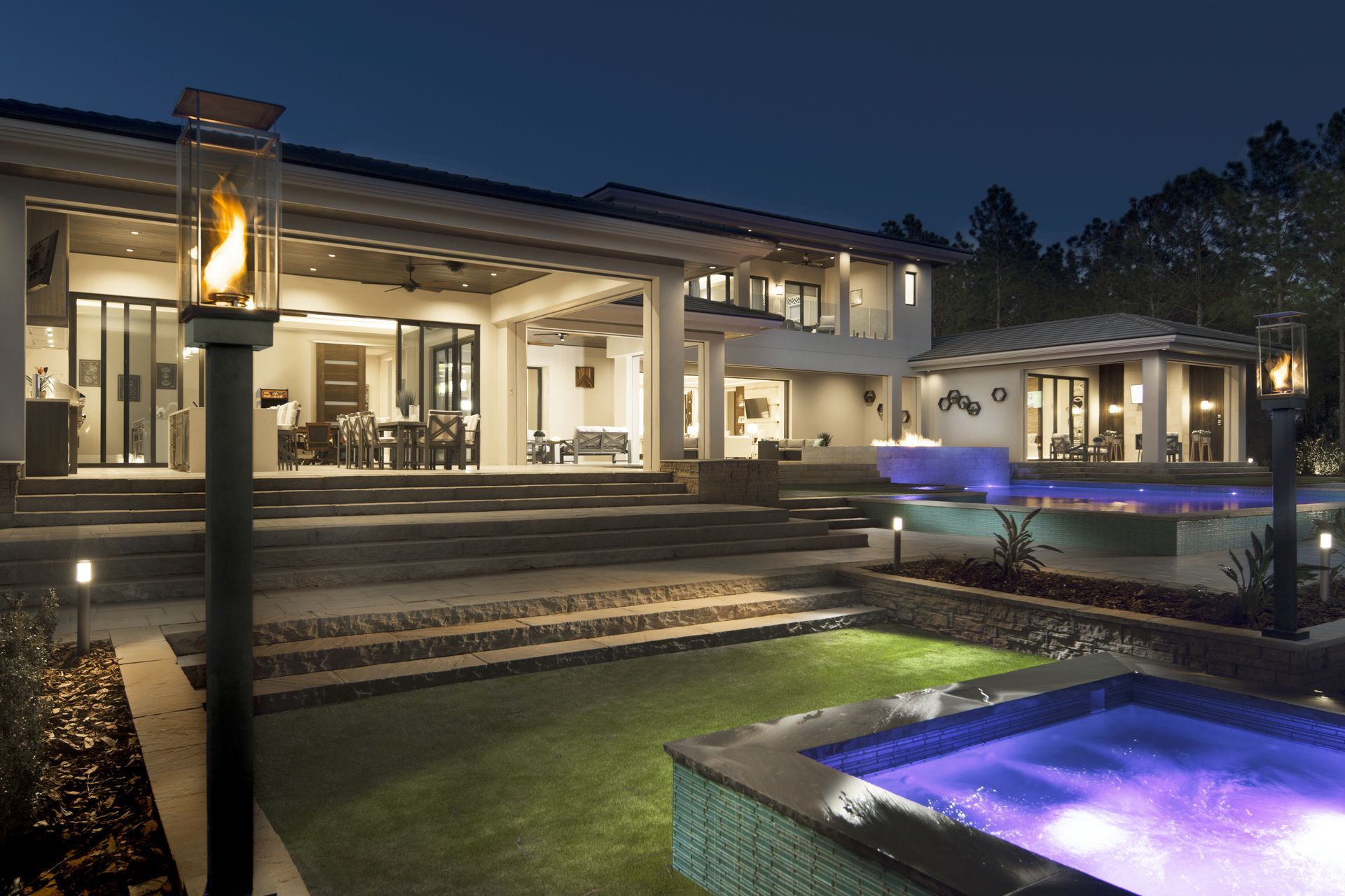 Modern house exterior at night with illuminated pool and patio lights
