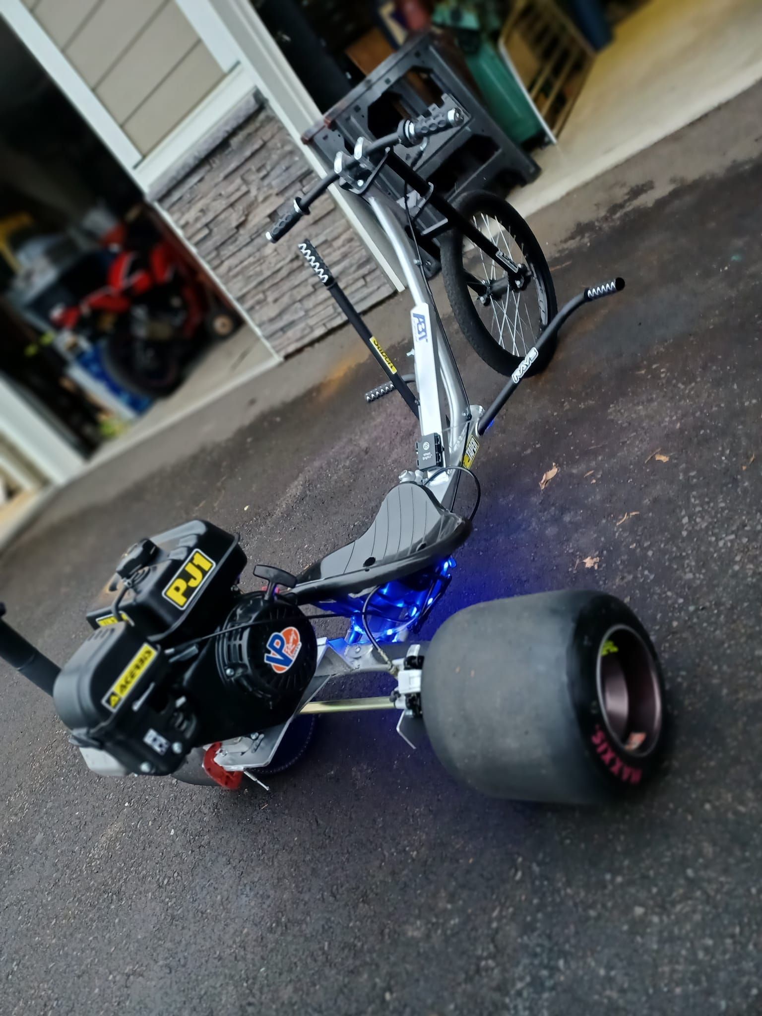 A drift trike is parked in a driveway next to a garage.