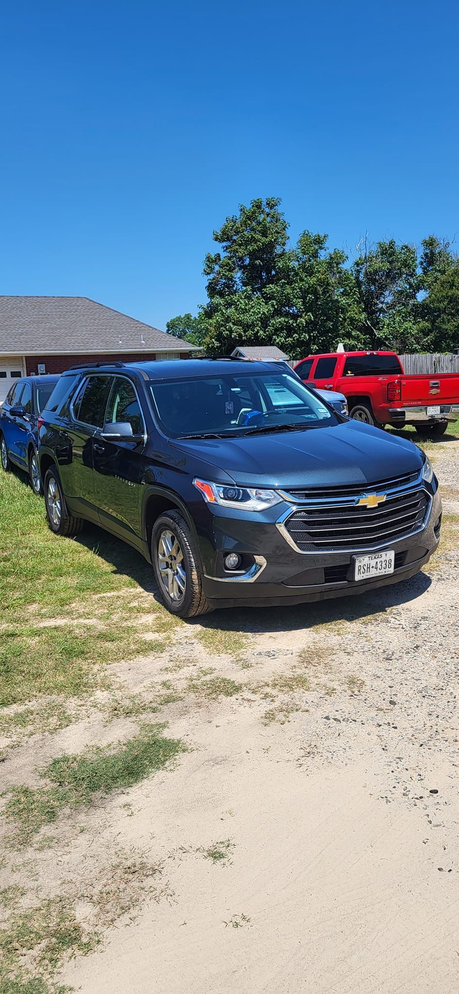 Dark SUV parked on a gravel driveway with a blue sky, grass, and trees in the background.