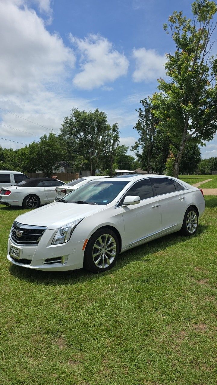 White Cadillac sedan parked on green grass, blue sky with puffy clouds in the background.